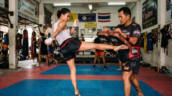 Peleador de Muay Thai lanzando una patada circular de espinilla contra un pao