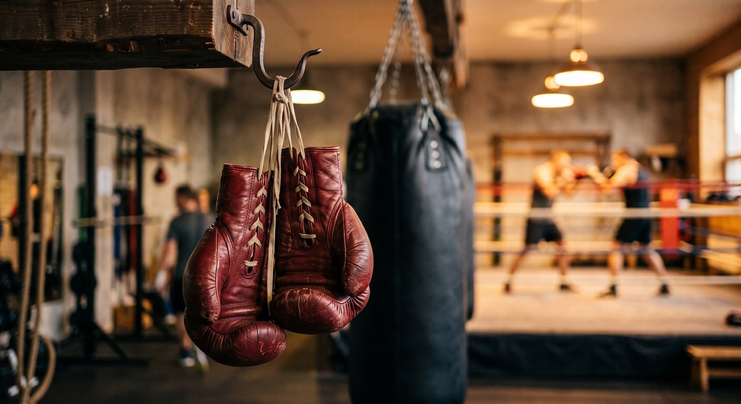 Guantes de boxeo de cuero colgados en un gimnasio, con un saco pesado al fondo