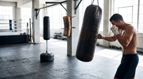 Gimnasio de boxeo con sacos colgante, de pie y de pared y un boxeador entrenando